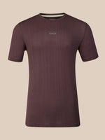 A dark brown short-sleeve athletic t-shirt with a subtle vertical ribbed texture, featuring a small multicolor logo on the center chest and a light green inner collar lining, shown against a solid beige background.