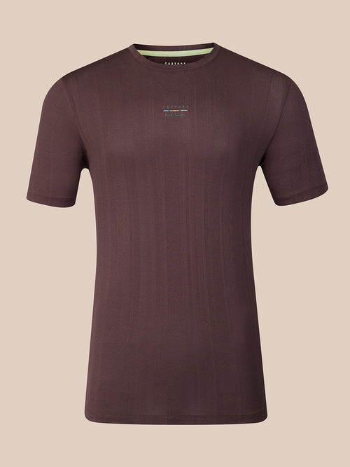 A dark brown short-sleeve athletic t-shirt with a subtle vertical ribbed texture, featuring a small multicolor logo on the center chest and a light green inner collar lining, shown against a solid beige background.