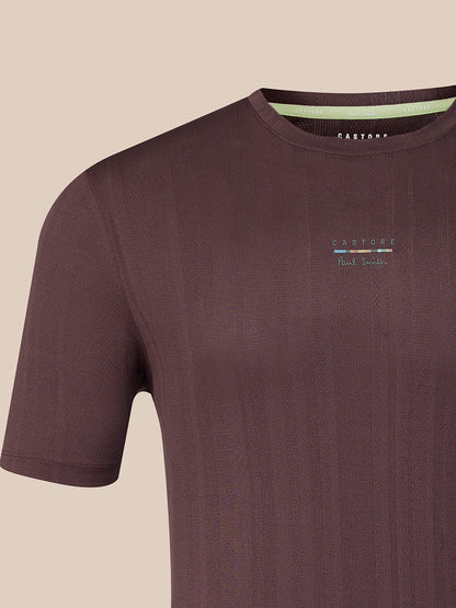 A close-up of a dark brown ribbed short-sleeve t-shirt with a small multicolor logo on the left chest and a light green inner collar lining. The brand name 'CASTORE' is visible on the inner neck label and chest.