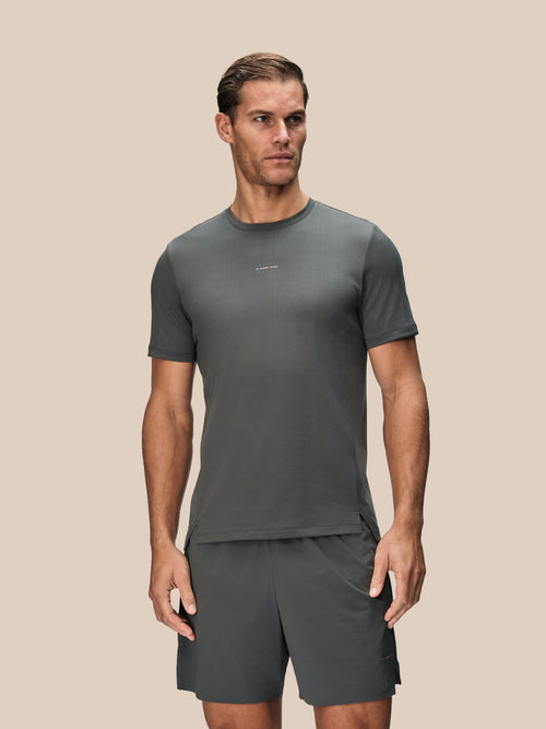 A man modeling a dark gray athletic t-shirt and matching shorts against a solid beige background.