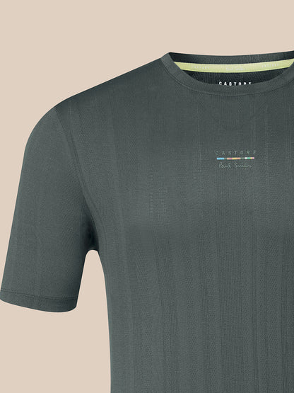 A close-up of a dark gray short-sleeve t-shirt with a ribbed texture, featuring a small multicolor logo on the chest and a light green inner collar lining. The brand name 'CASTORE' is visible inside the collar.