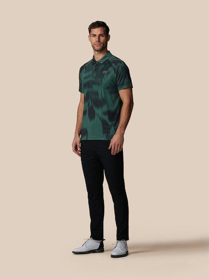 Man wearing a green camouflage polo shirt and black pants on a beige background