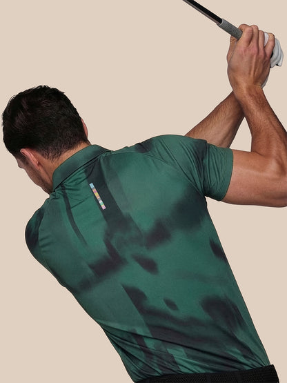 Man in a green patterned shirt swinging a golf club against a beige background