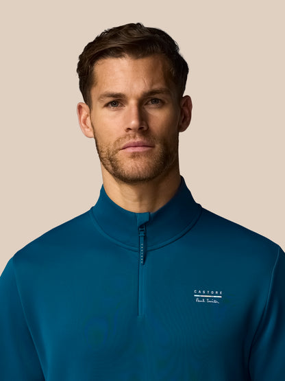 Man wearing a blue quarter-zip sweatshirt with a brand logo on a beige background