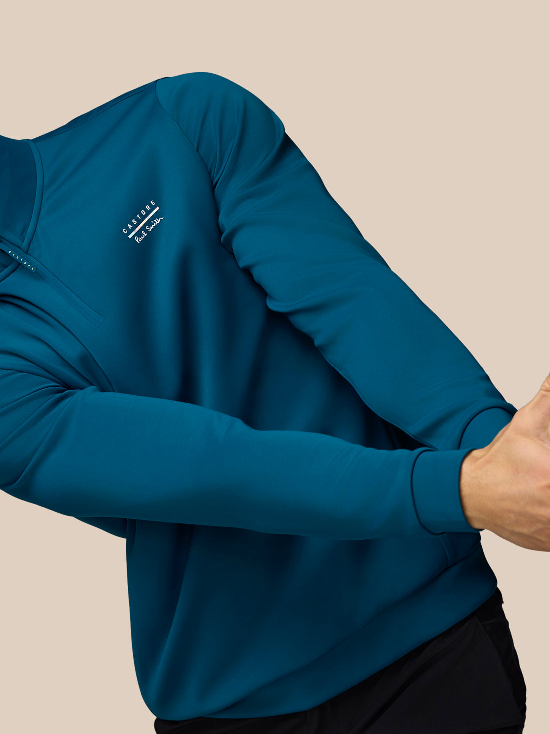 Person wearing a blue long-sleeve shirt with a brand logo on a beige background