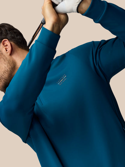Man wearing a blue sweatshirt with a logo, holding a white object against a beige background