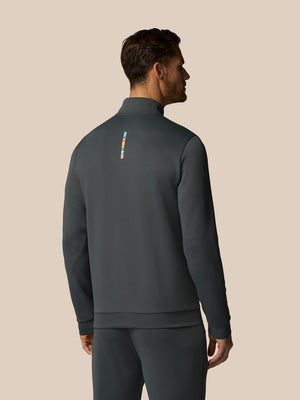 Man wearing a dark gray athletic jacket with a small logo on the back against a beige background