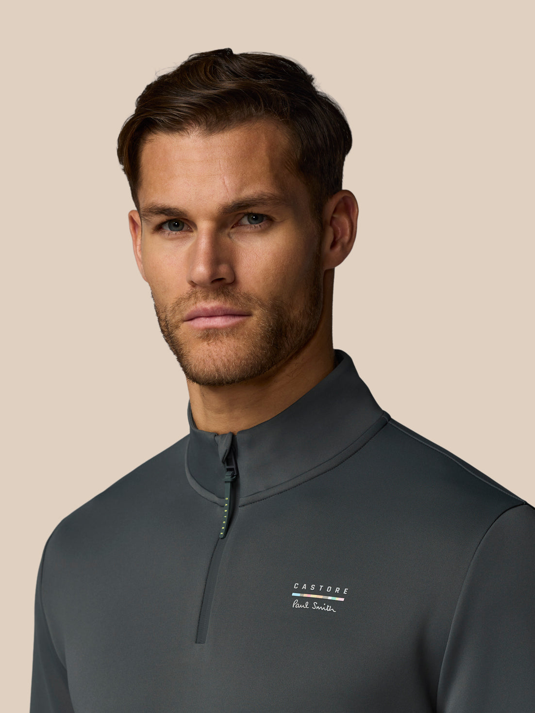 Man wearing a dark gray quarter-zip shirt with a brand logo on a beige background