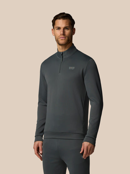 Man wearing a dark gray pullover with a small logo on a beige background