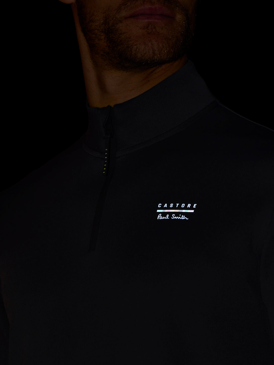 Close-up of a person wearing a dark jacket with a brand logo on a black background