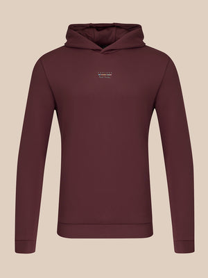 A dark plum-colored long-sleeve hoodie with a small white embroidered logo on the left chest, displayed on a neutral beige background.