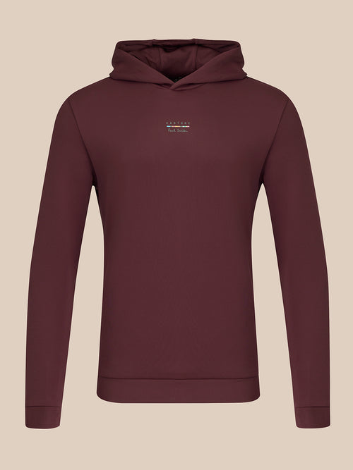 A dark plum-colored long-sleeve hoodie with a small white embroidered logo on the left chest, displayed on a neutral beige background.