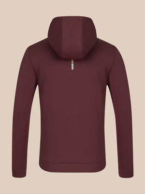 A dark plum-colored zip-up hoodie shown from the back, featuring a small vertical metallic zipper pull with a colorful logo, set against a solid beige background.