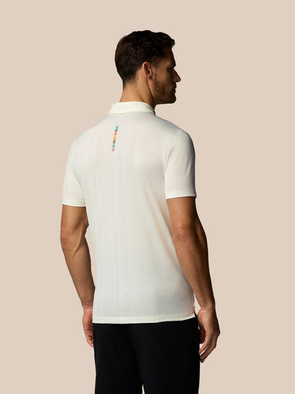 Man wearing a white polo shirt with a colorful logo on the back against a beige background