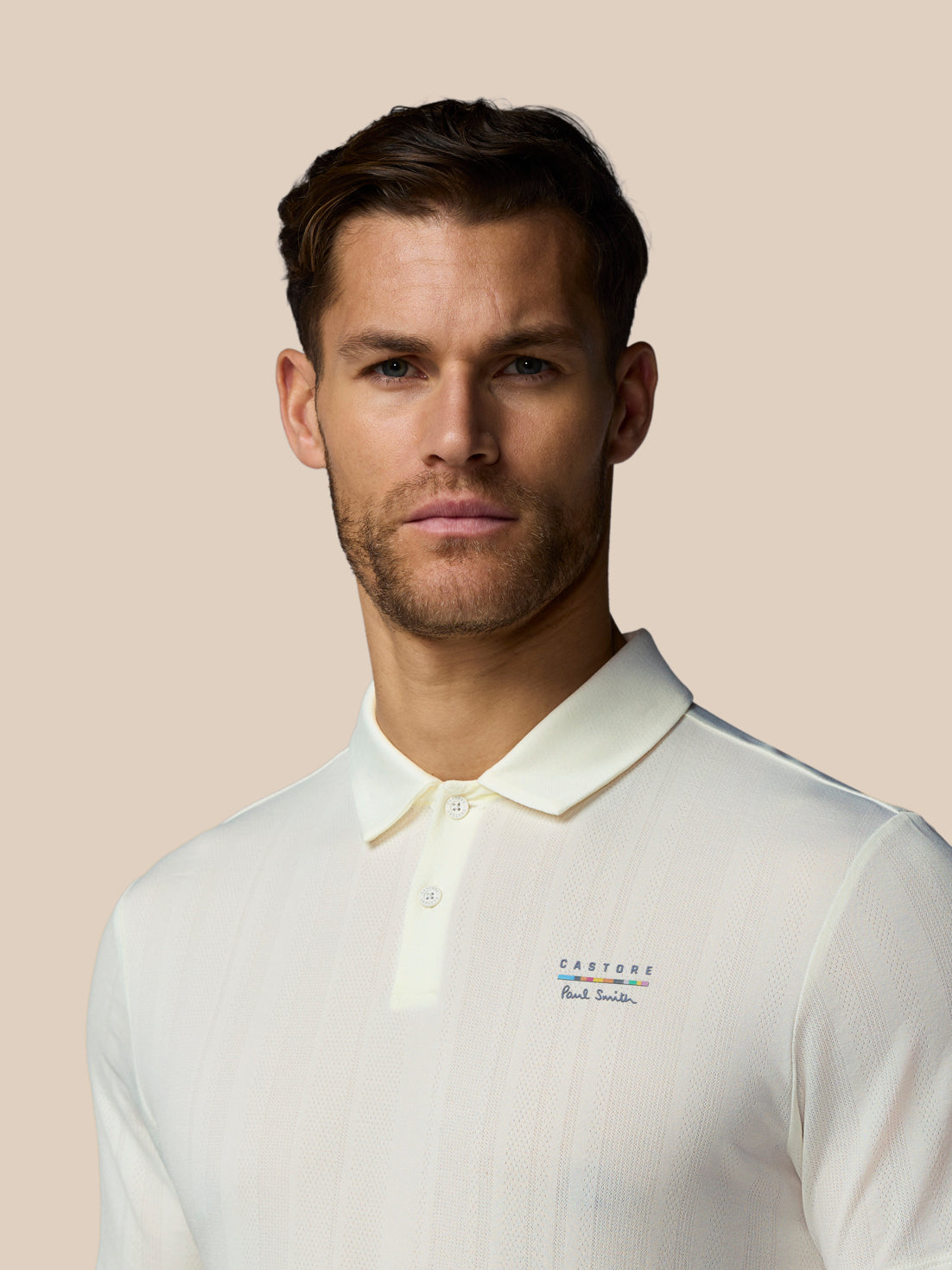 Man wearing a white polo shirt with brand logos on a beige background