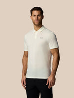 Man wearing a white polo shirt with a logo on a beige background