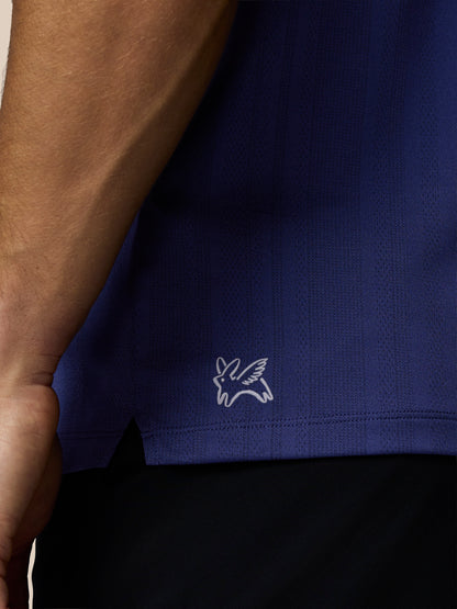 Close-up of a blue polo shirt with a white logo on a beige background