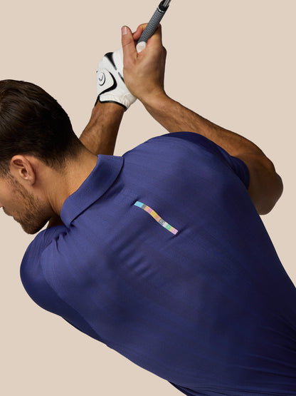 Man in a blue polo shirt holding a golf club against a beige background