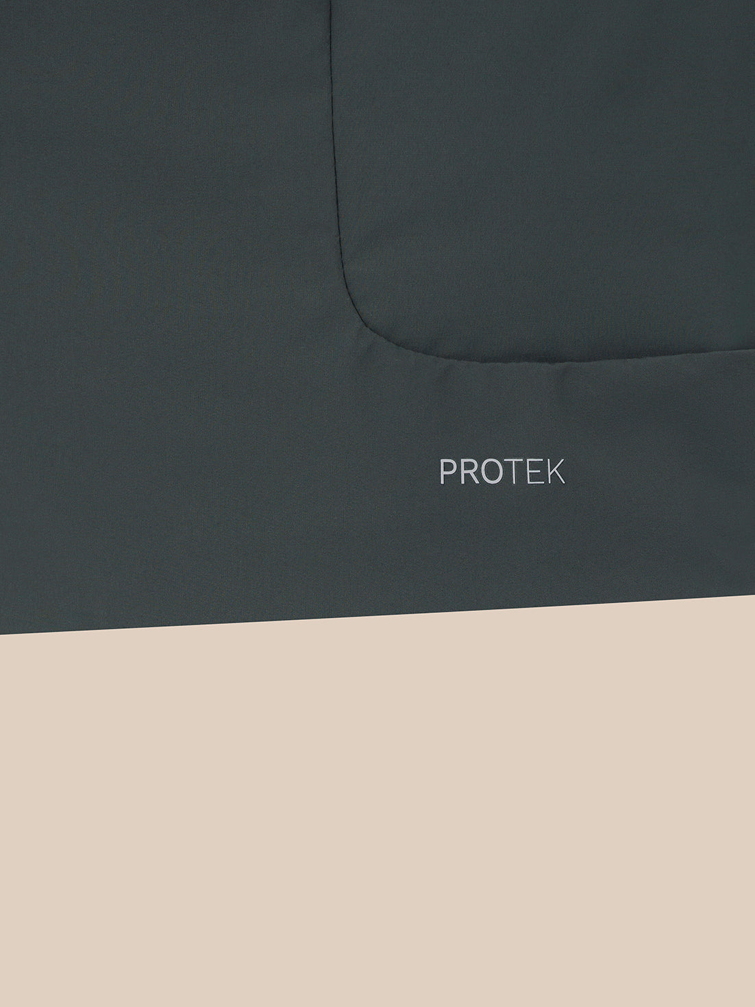 Close-up of a dark charcoal gray fabric surface with a curved seam and the word PROTEK printed in small white text, with the lower half of the frame filled with a light beige block.