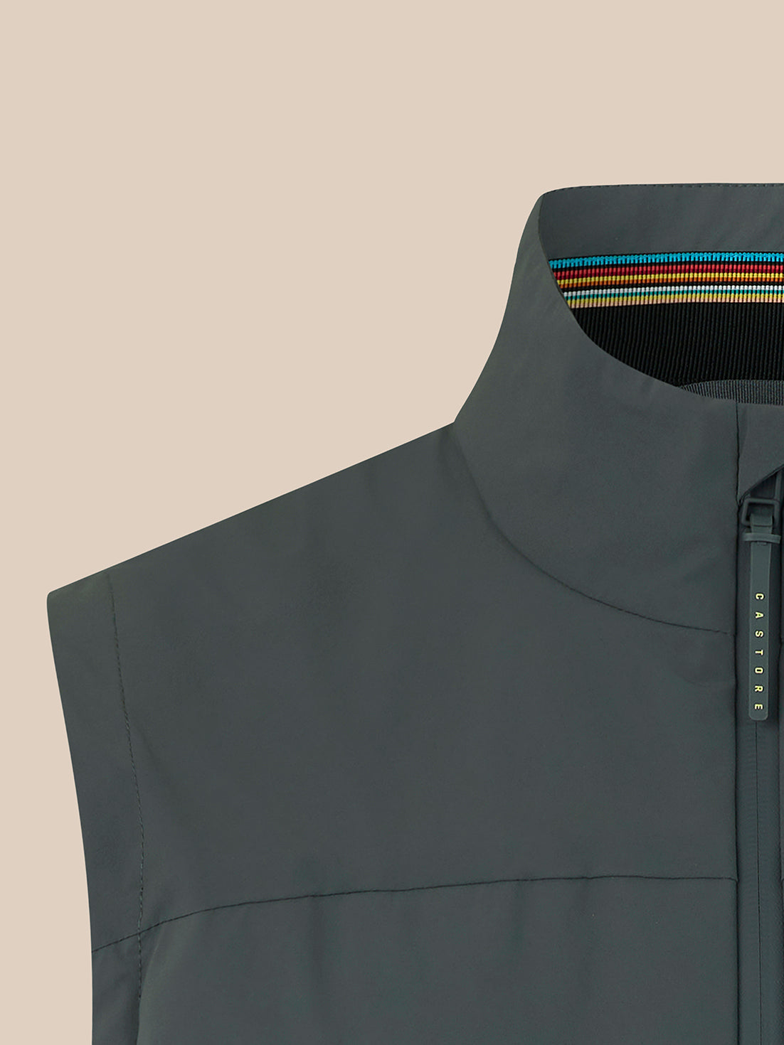 Close-up of a dark gray sleeveless zip-front vest with a high stand collar, shown against a plain beige background. A small vertical brand tab on the zipper reads CASTORE.