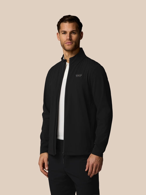 Man wearing a black jacket with a logo on a beige background
