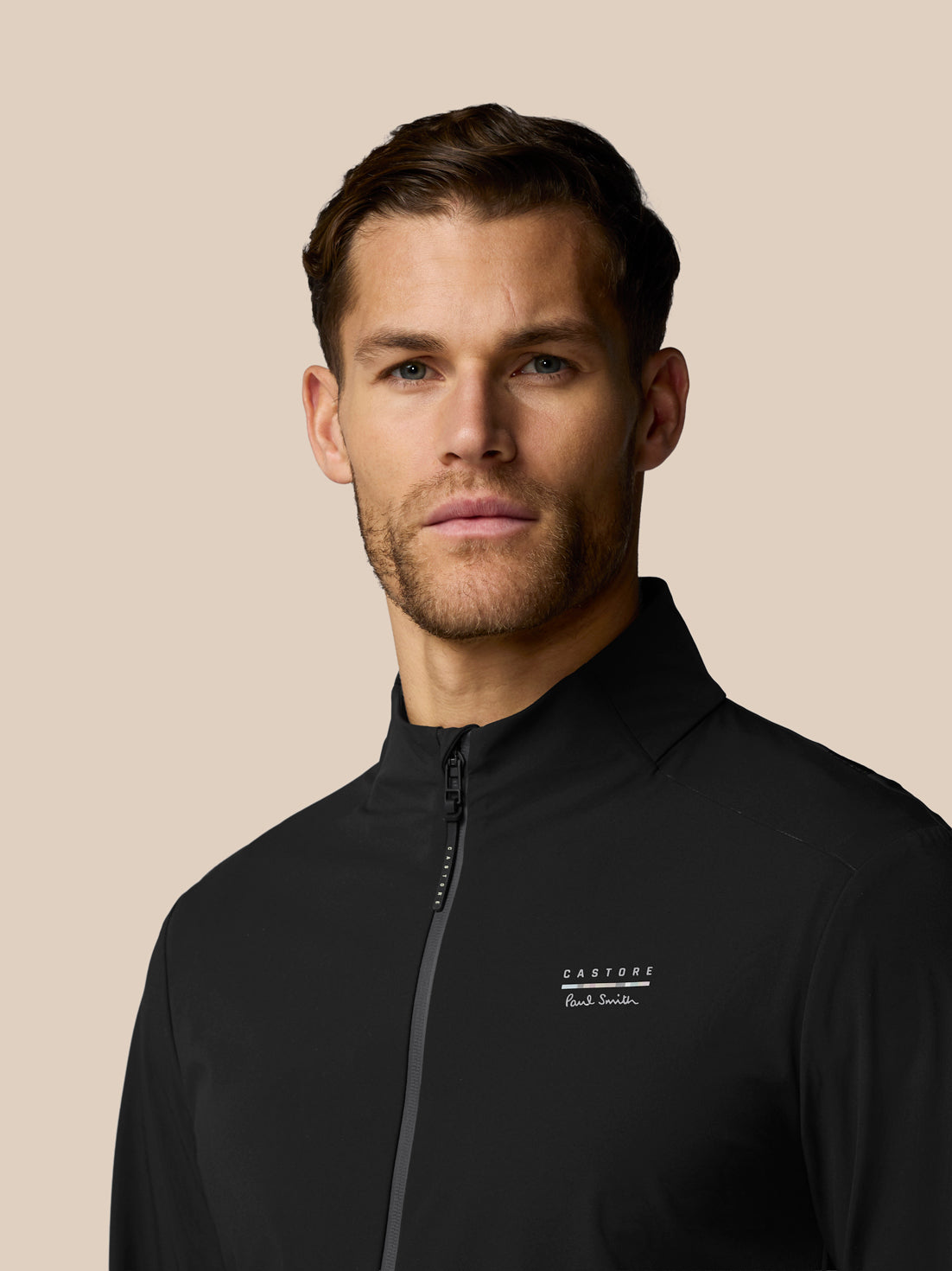 Man wearing a black jacket with a brand logo on a beige background