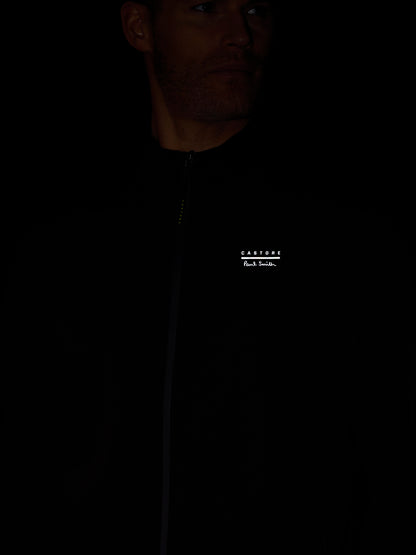 Person wearing a black jacket with a brand logo on a dark background