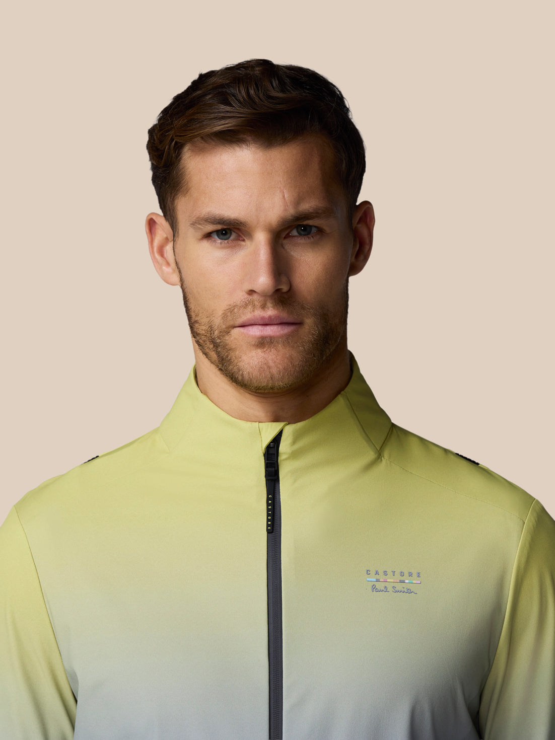 Man wearing a light green jacket with a brand logo on a beige background