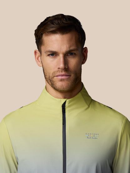 Man wearing a light green jacket with a brand logo on a beige background