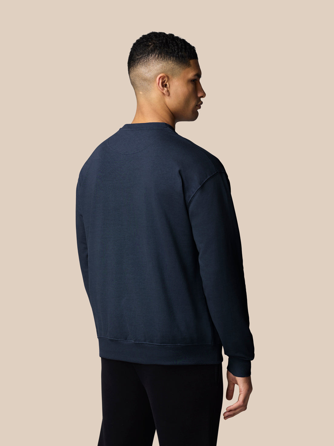 Back view of a male model in navy Adapt Lifestyle Sweatshirt showing an oversized silhouette and ribbed cuffs and hem