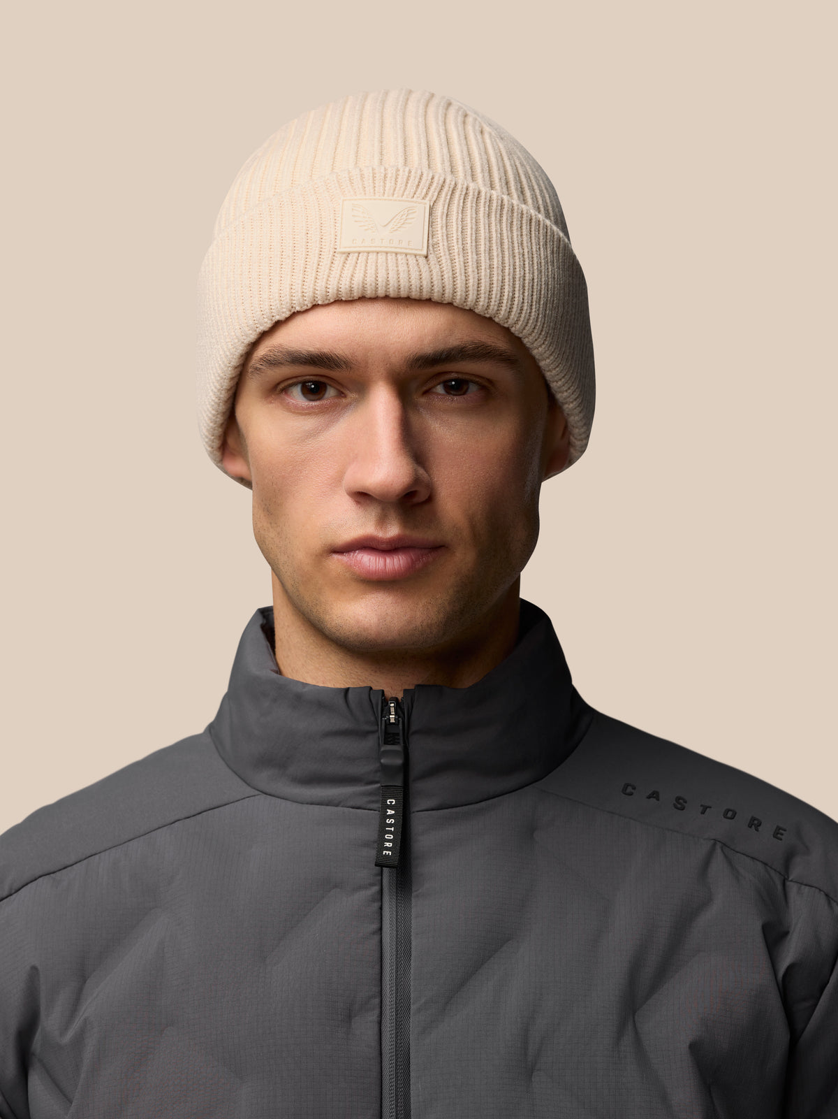 Stone colored ribbed knit Active Beanie with Castore logo at the fold worn by a male model.