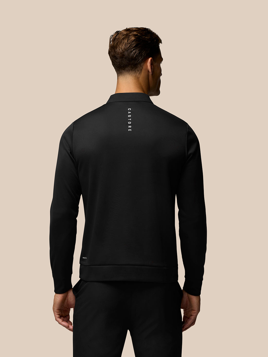Back view of a man in a black Castore golf top with a vertical logo down the back