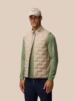 Male model wearing Mushroom Golf Pinnacle Gilet over a green long sleeve, showing the quilted front and funnel collar.