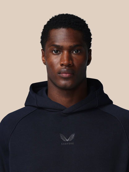 Man wearing a navy hoodie with a logo on a beige background
