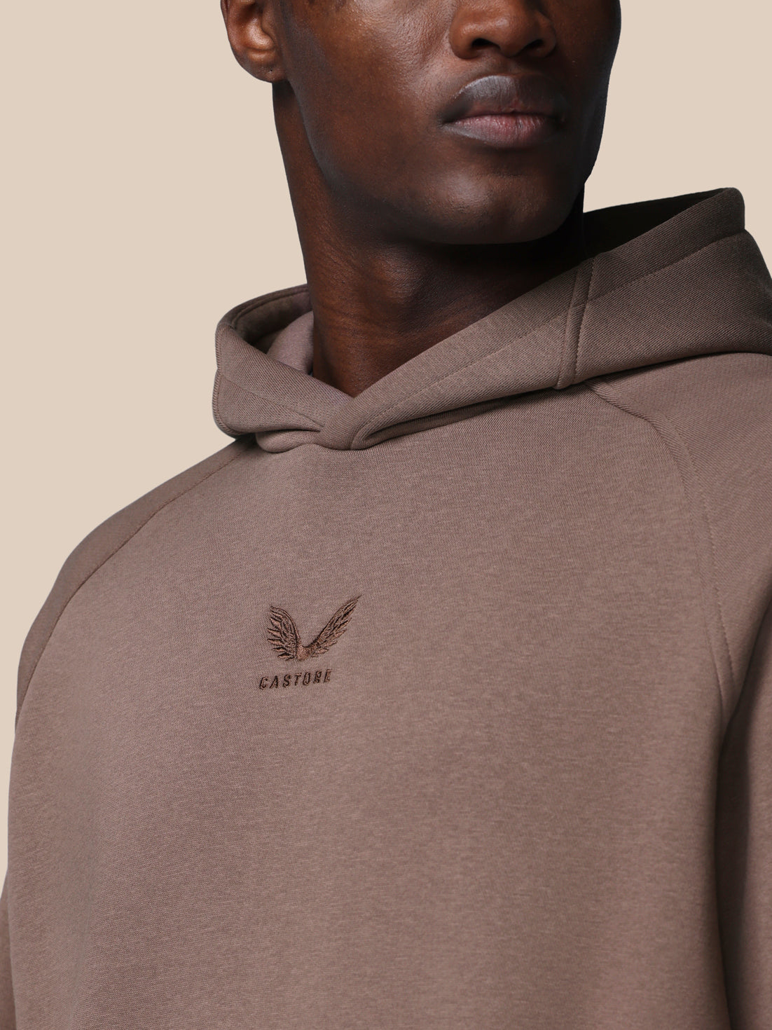 Brown hoodie with a logo on the chest against a beige background