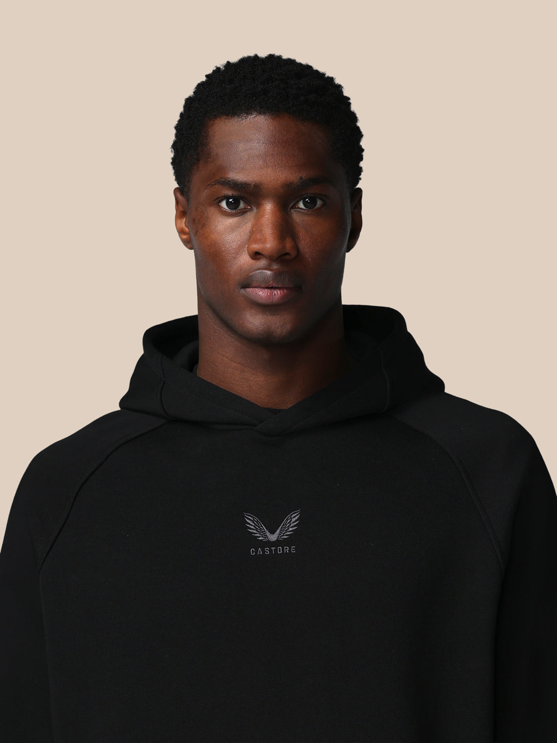 Man wearing a black hoodie with a logo on a beige background
