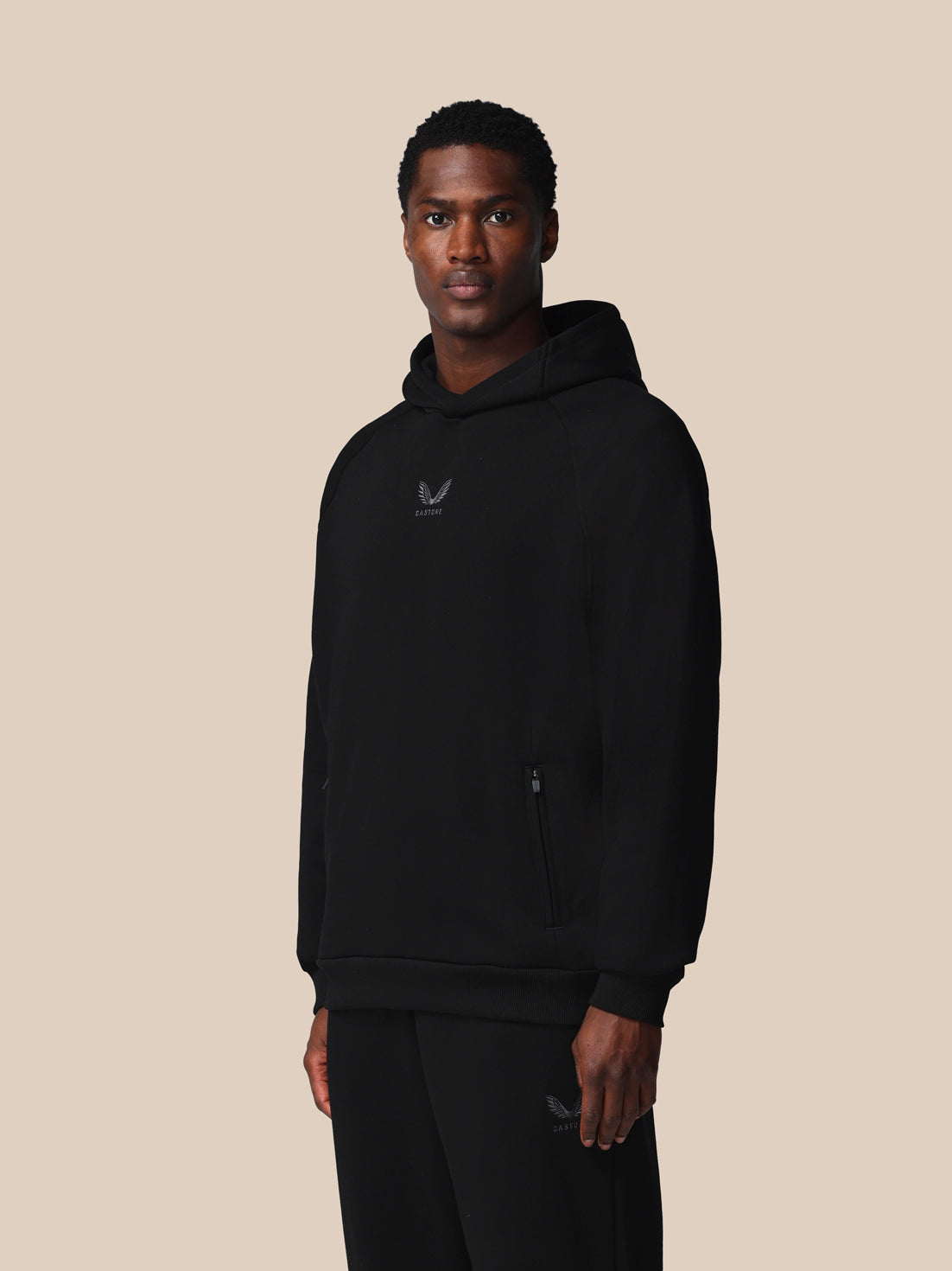 Person wearing a black hoodie with a logo on a beige background