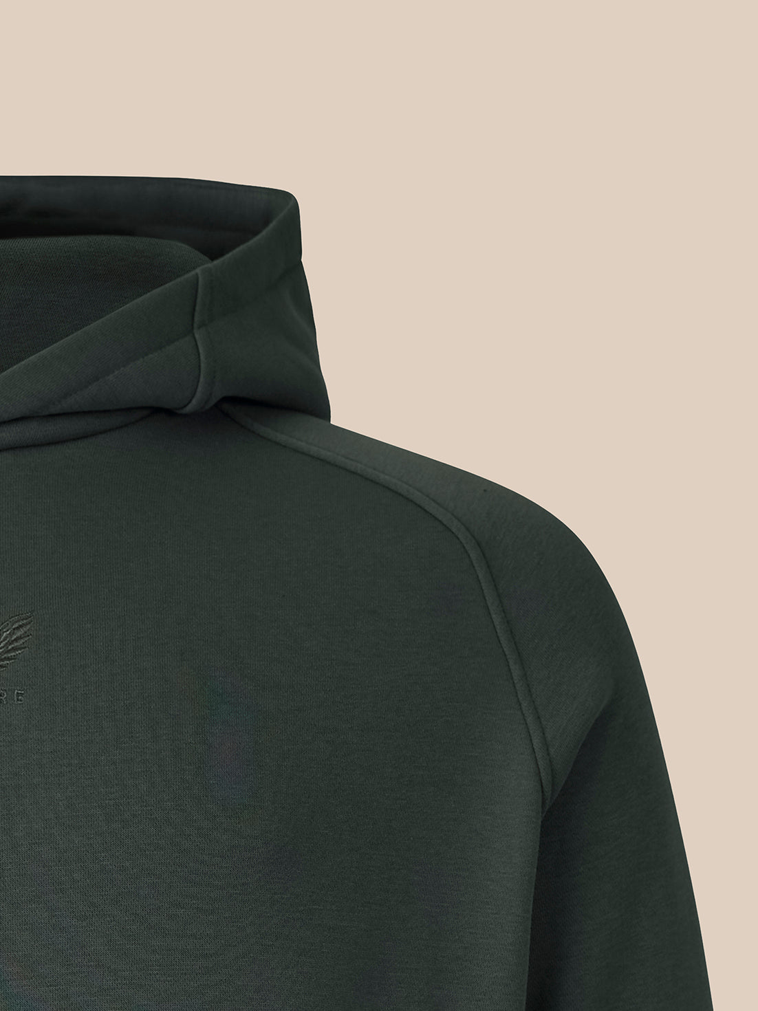 Close-up of a dark forest green hooded sweatshirt showing the shoulder, sleeve, and hood against a solid beige background.