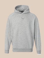 A light gray heather pullover hoodie with a small dark gray winged logo on the center chest, displayed against a solid beige background.