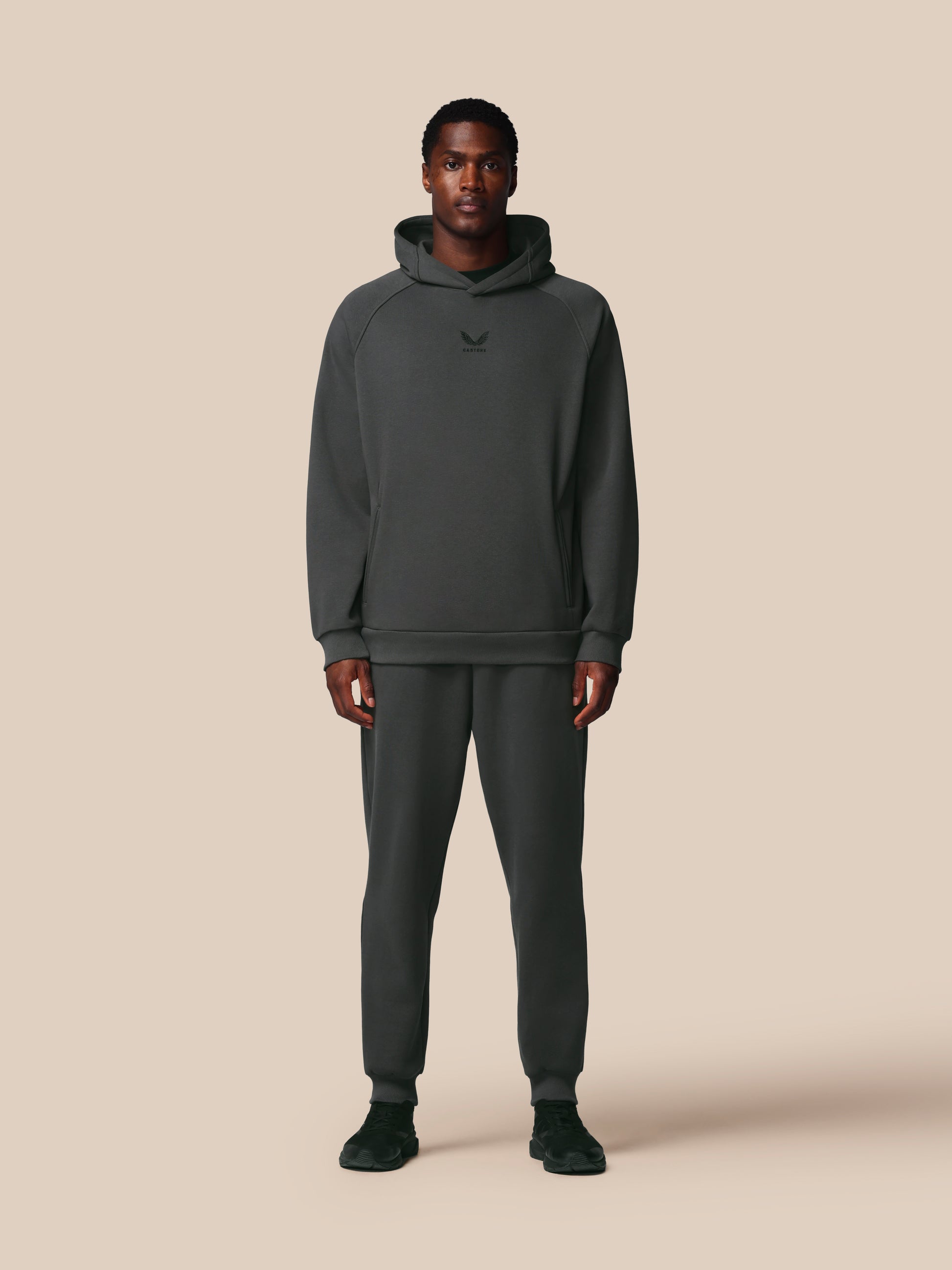 Person wearing a dark gray hoodie and pants on a beige background