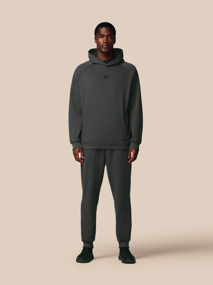Person wearing a dark gray hoodie and pants on a beige background