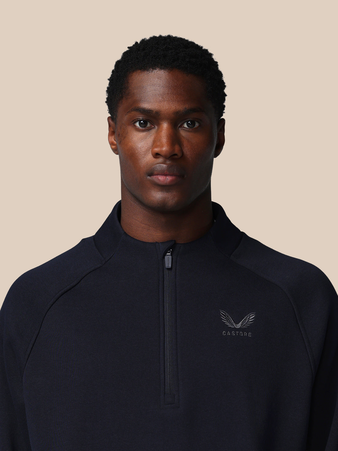 Man wearing a black quarter-zip sweatshirt with a logo on a beige background