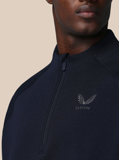 Person wearing a black quarter-zip sweatshirt with a brand logo on a beige background