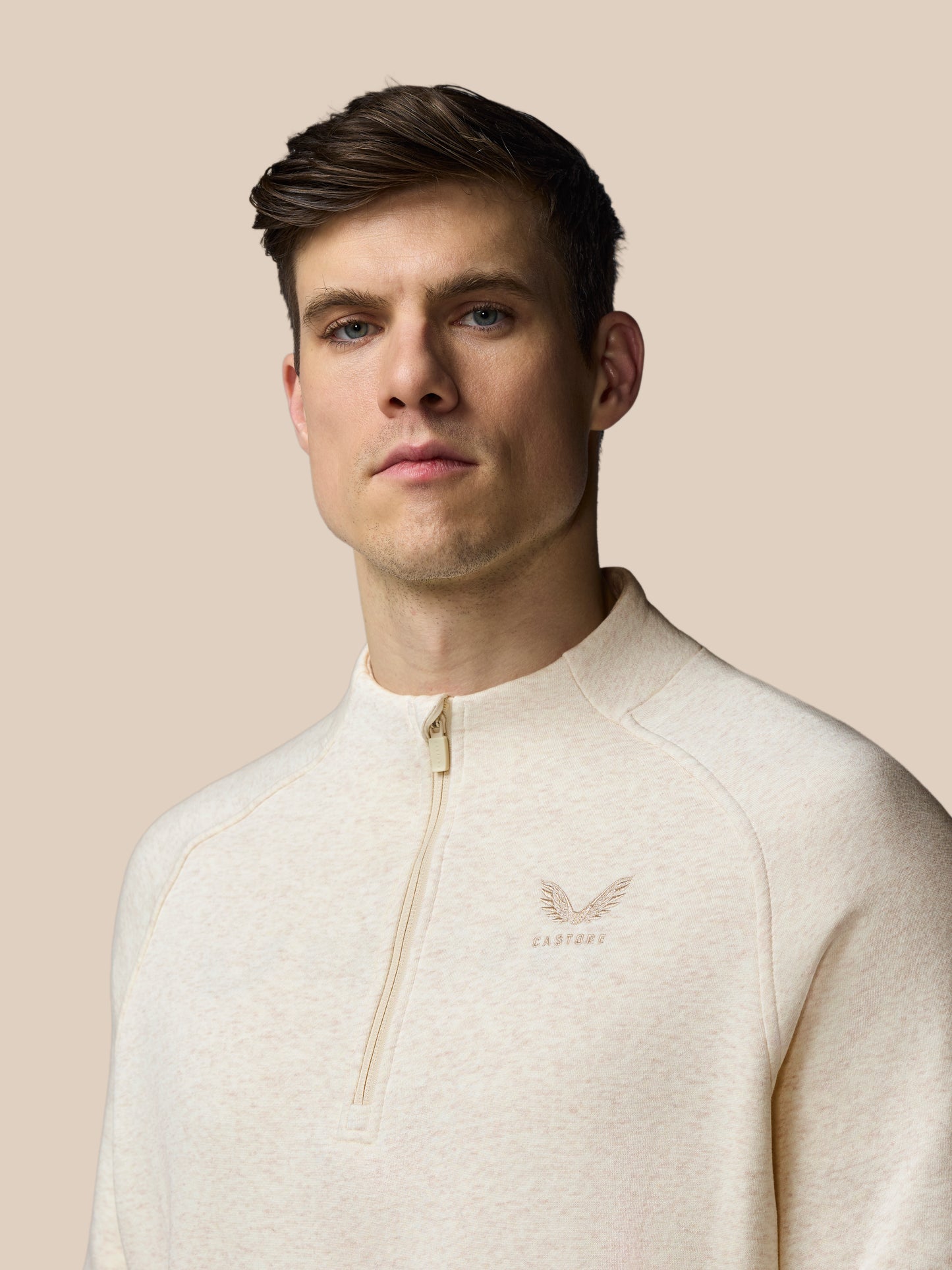 Man wearing a cream-colored sweater with a brand logo on a beige background