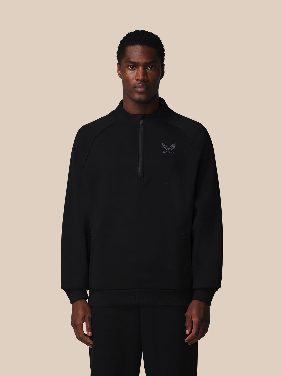 Person wearing a black zip-up sweatshirt with a logo on a beige background