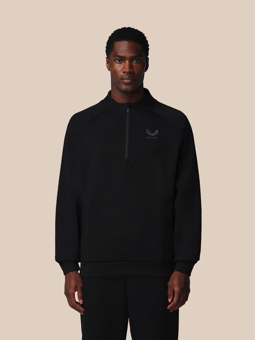 Person wearing a black zip-up sweatshirt with a logo on a beige background