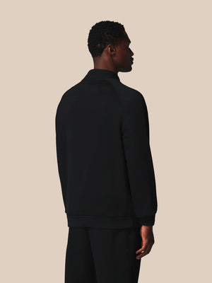 Person wearing a black half-zip sweatshirt and pants on a beige background