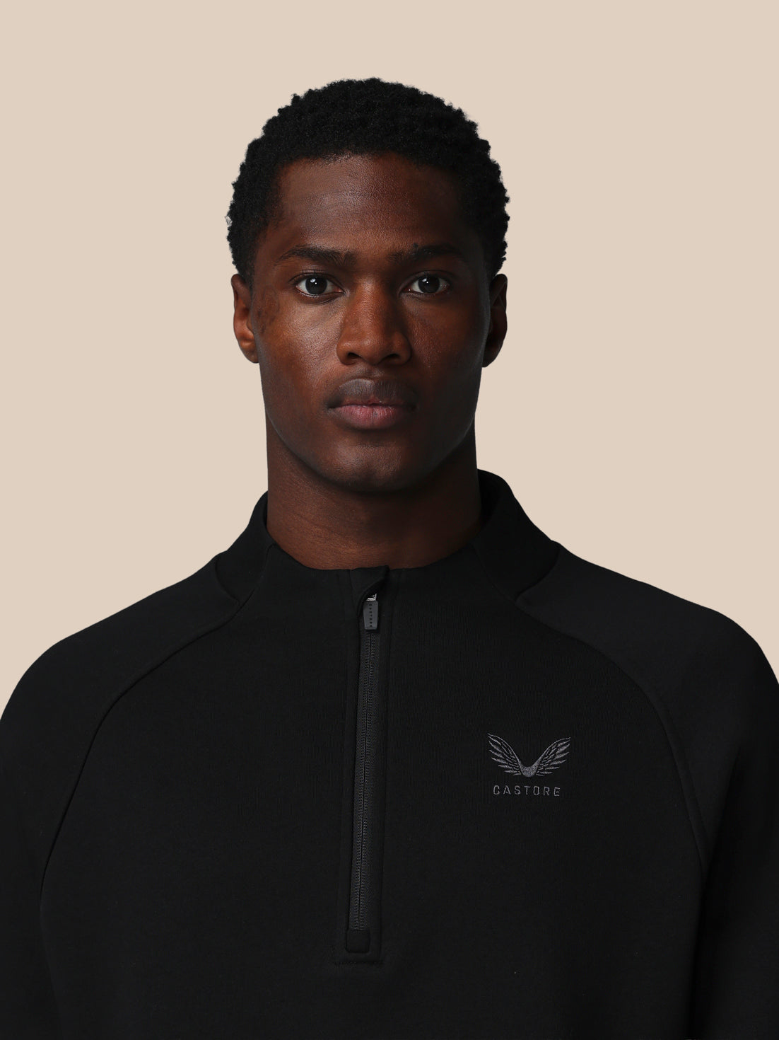 Man wearing a black jacket with a logo on a beige background