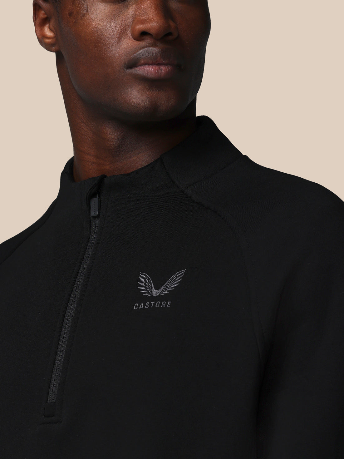 Person wearing a black jacket with a brand logo on a beige background