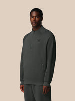 Man wearing a dark gray pullover with a small logo on a beige background